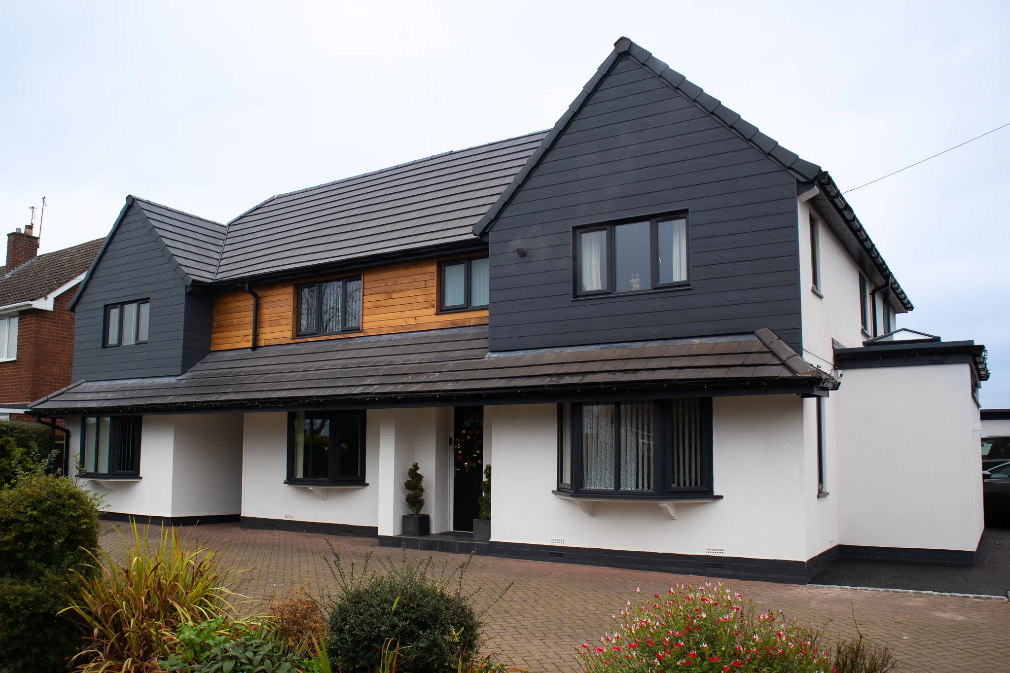 Front of a renovated home in Astwood Bank, in white render, dark cladding and timber