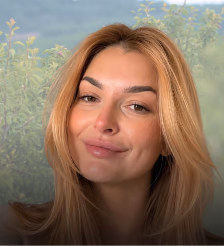 Smiling woman with long blonde hair against a blurred green outdoor background.