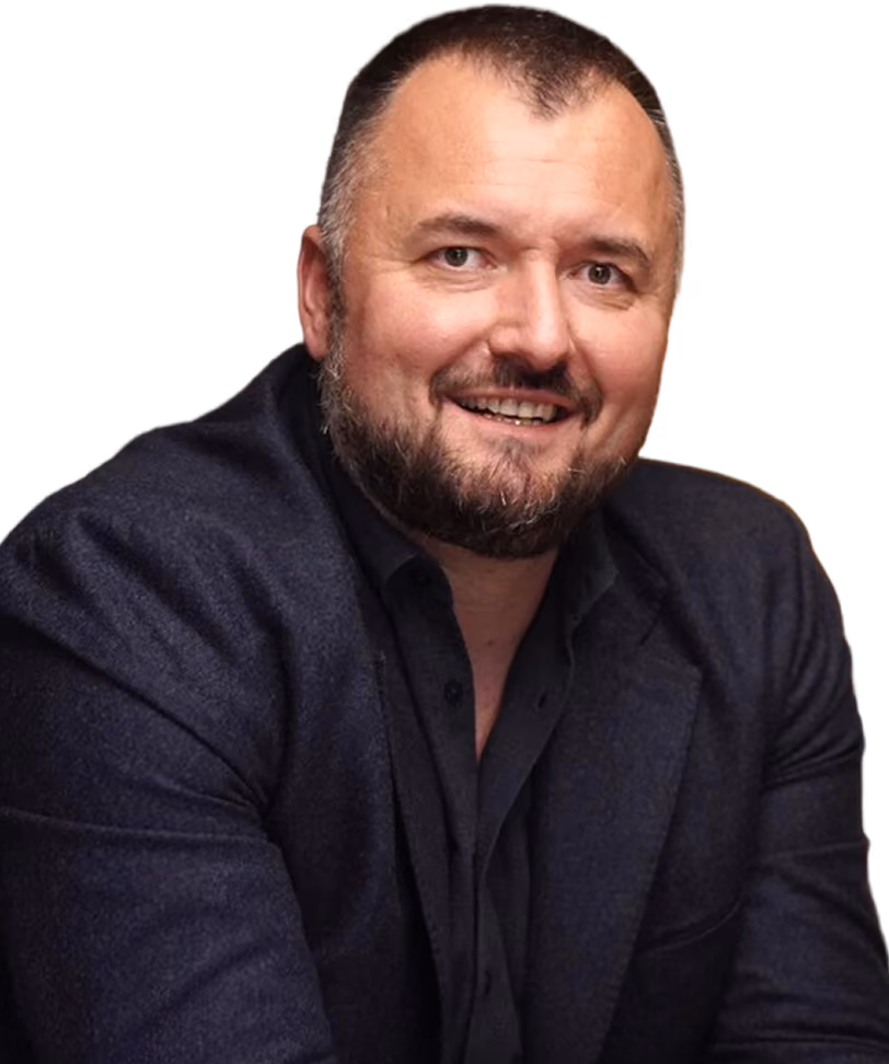 Smiling man with beard wearing a dark blazer and shirt against a transparent background.
