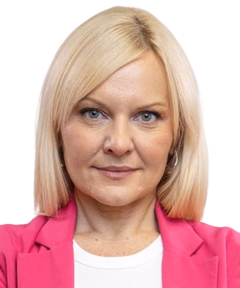 Blonde woman with blue eyes wearing a pink blazer and white shirt looking at the camera.