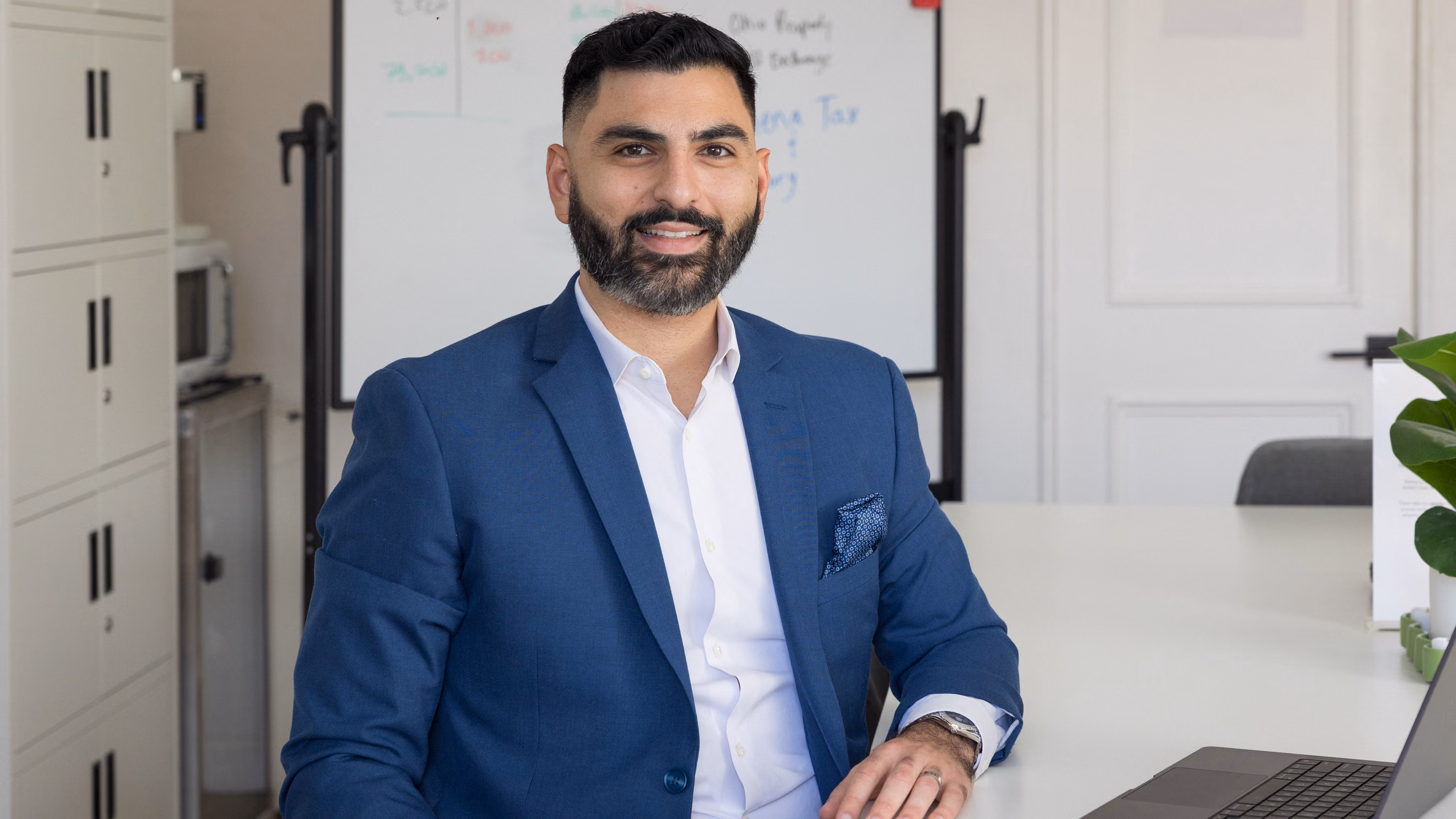 Edmond Petrosyan, founder of Athena Tax & Advisory, smiling at his desk with his laptop open