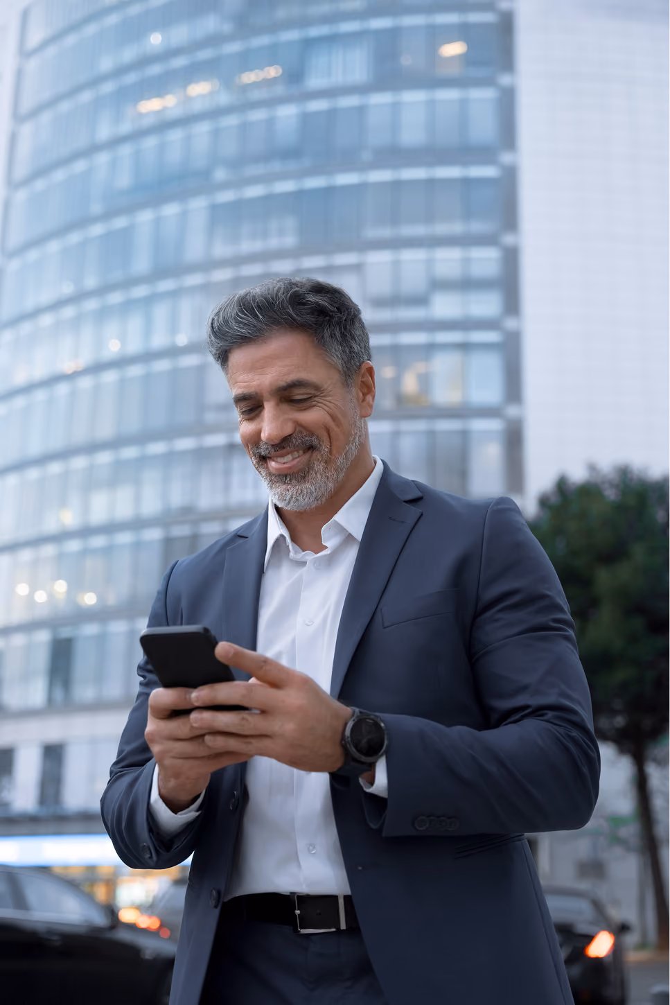 Business owner in a suit smiling while checking his phone on a city street