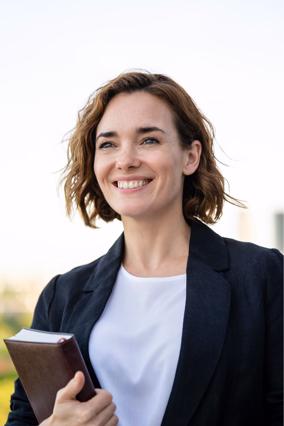Business owner in a blazer smiling outdoors while holding a notebook