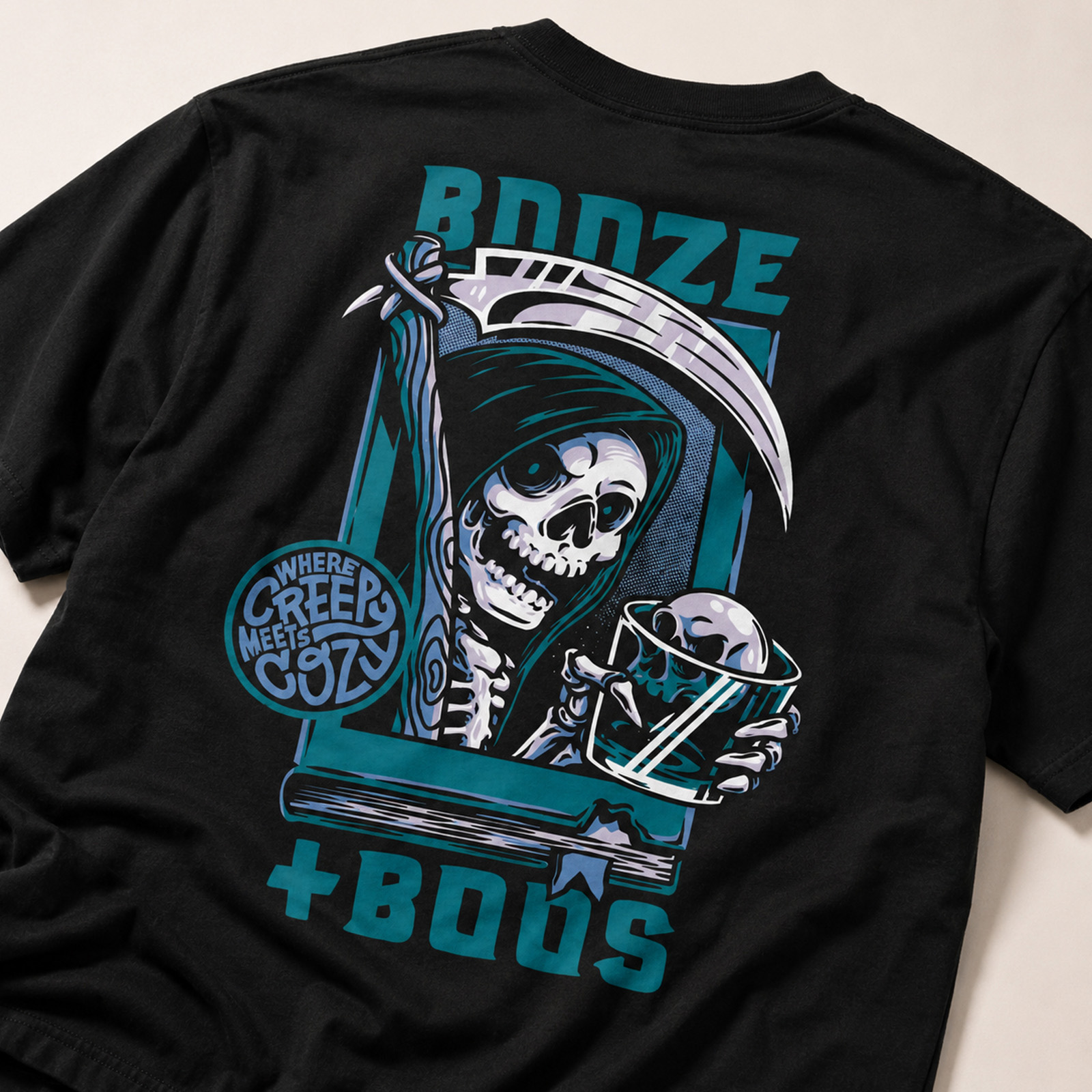 Black Booze + Boos T-shirt featuring an illustrated hooded skeleton with a scythe and drink alongside the “where creepy meets cozy” slogan.