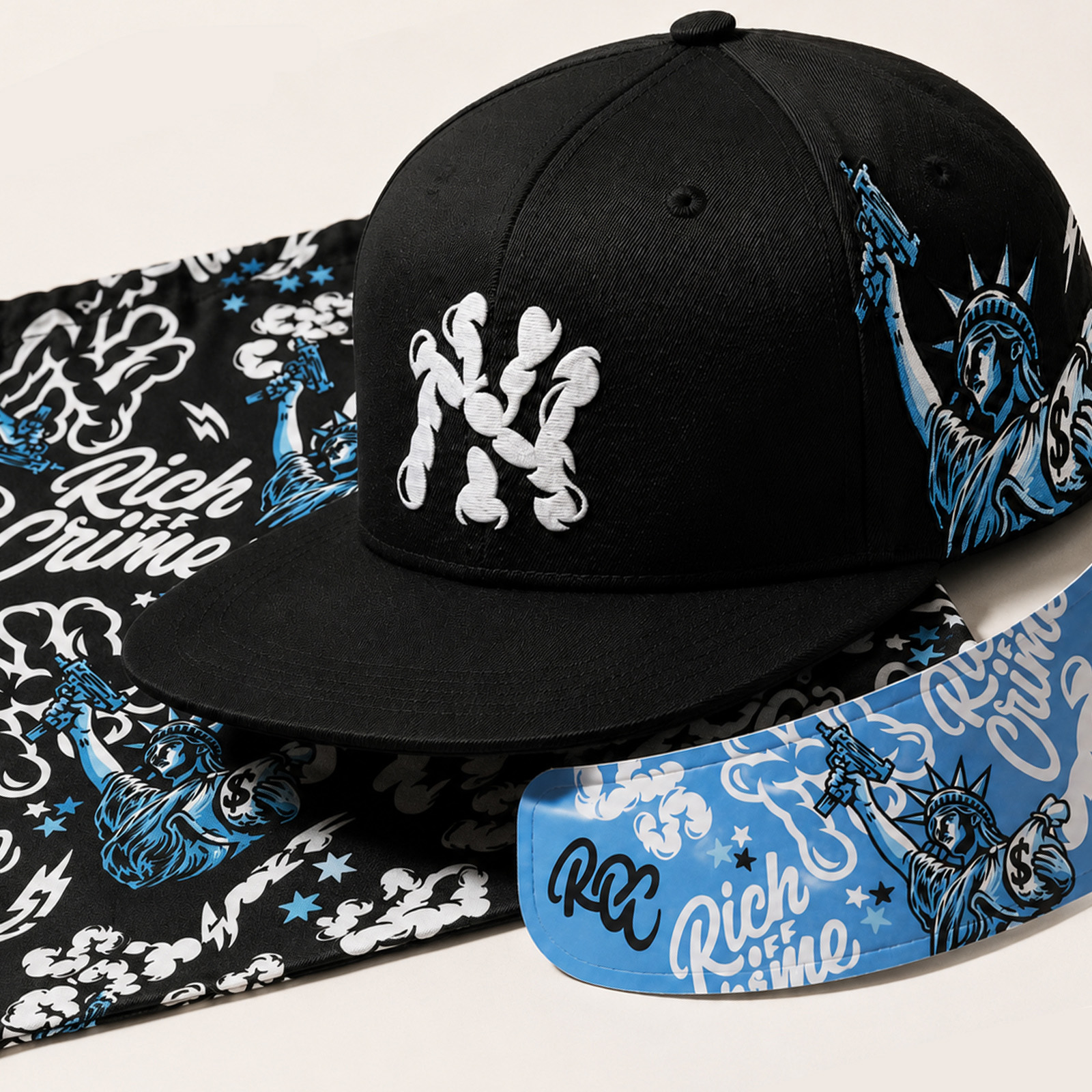 Close-up of a black Rich Off Crime cap with white embroidered lettering, blue Statue of Liberty artwork and matching printed accessories.
