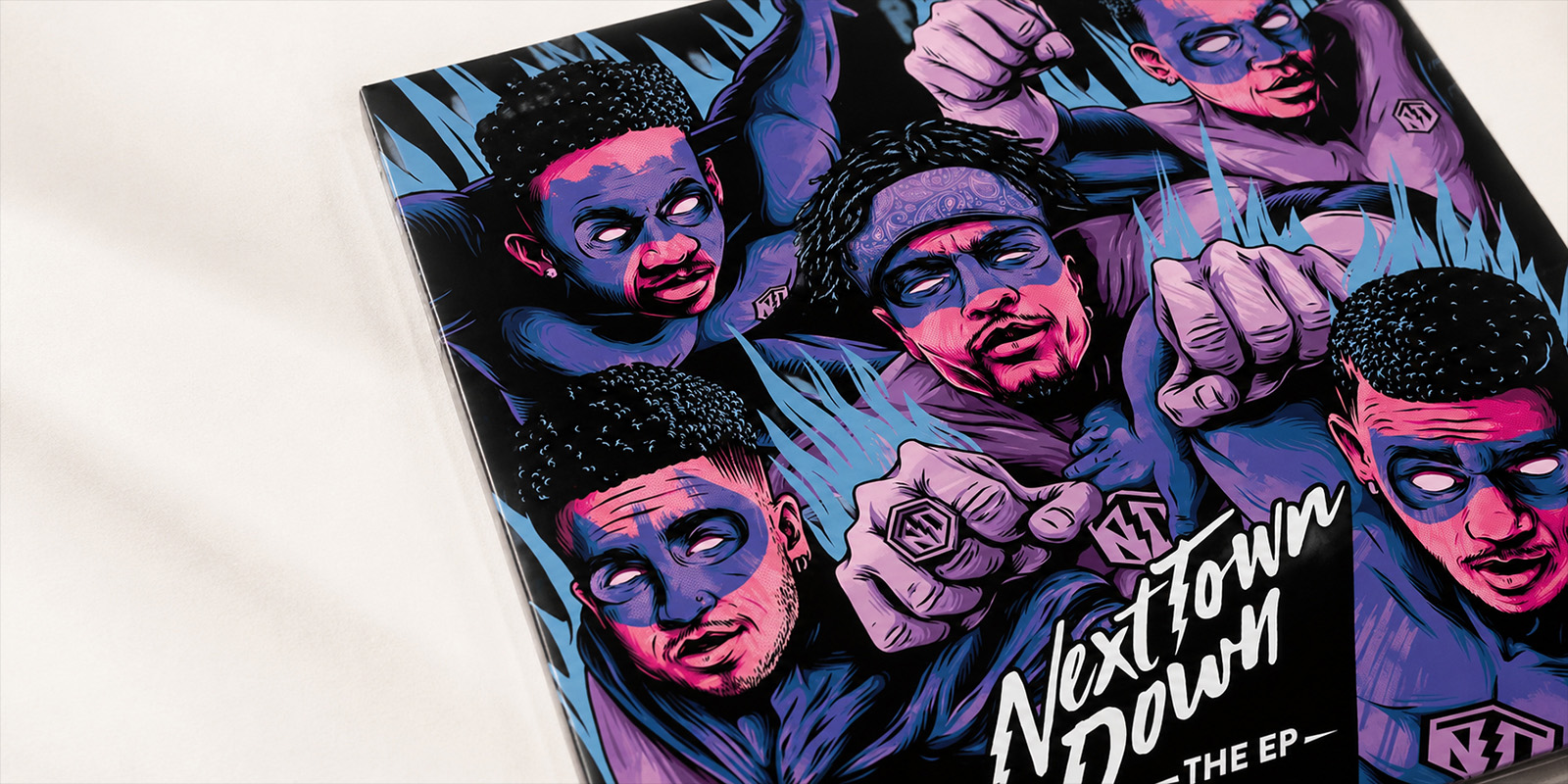 Printed Next Town Down EP cover photographed at an angle, featuring the full illustrated band artwork and custom NTD identity.