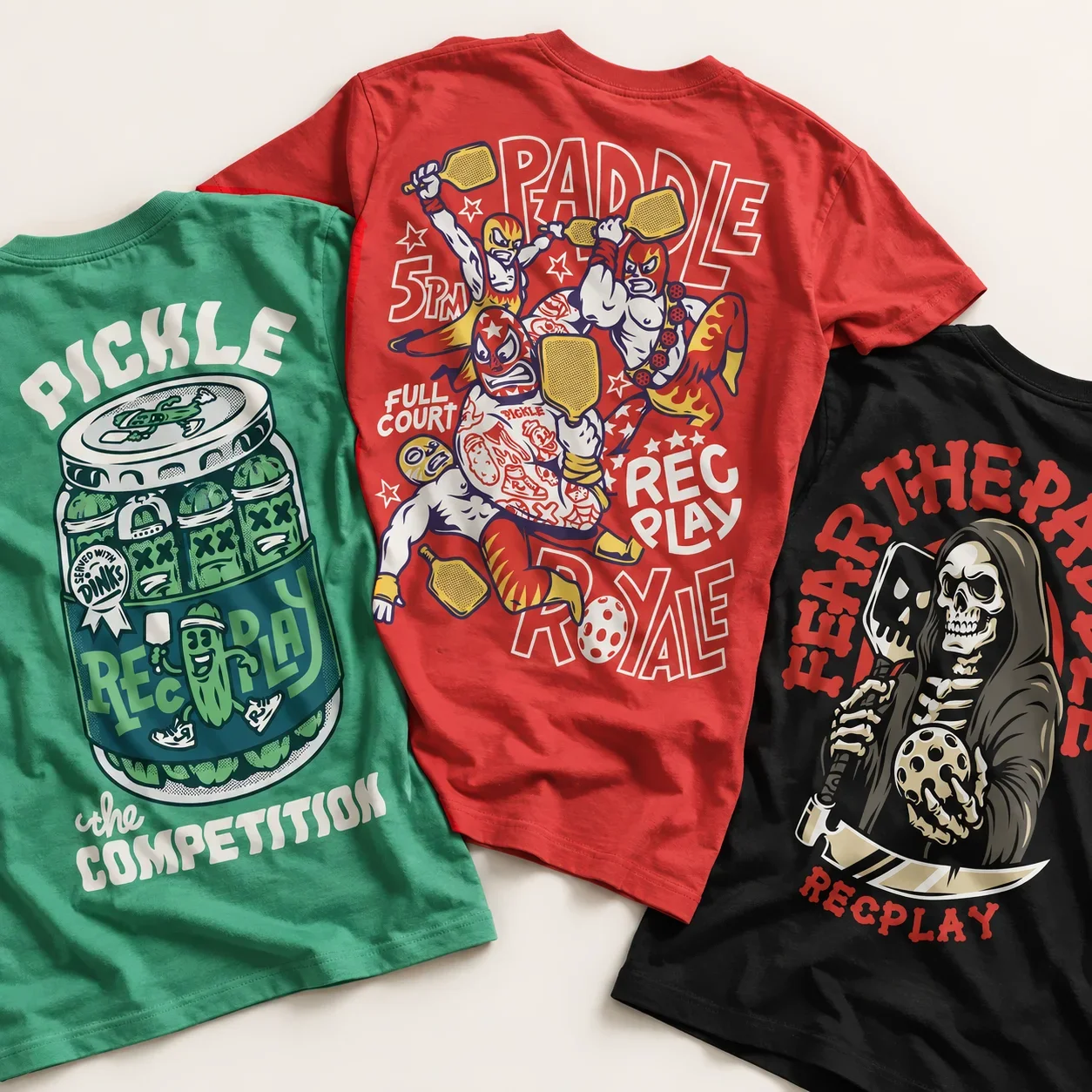 Three RecPLAY pickleball T-shirts featuring Pickle the Competition, Paddle Royale and Fear the Paddle illustrated designs.