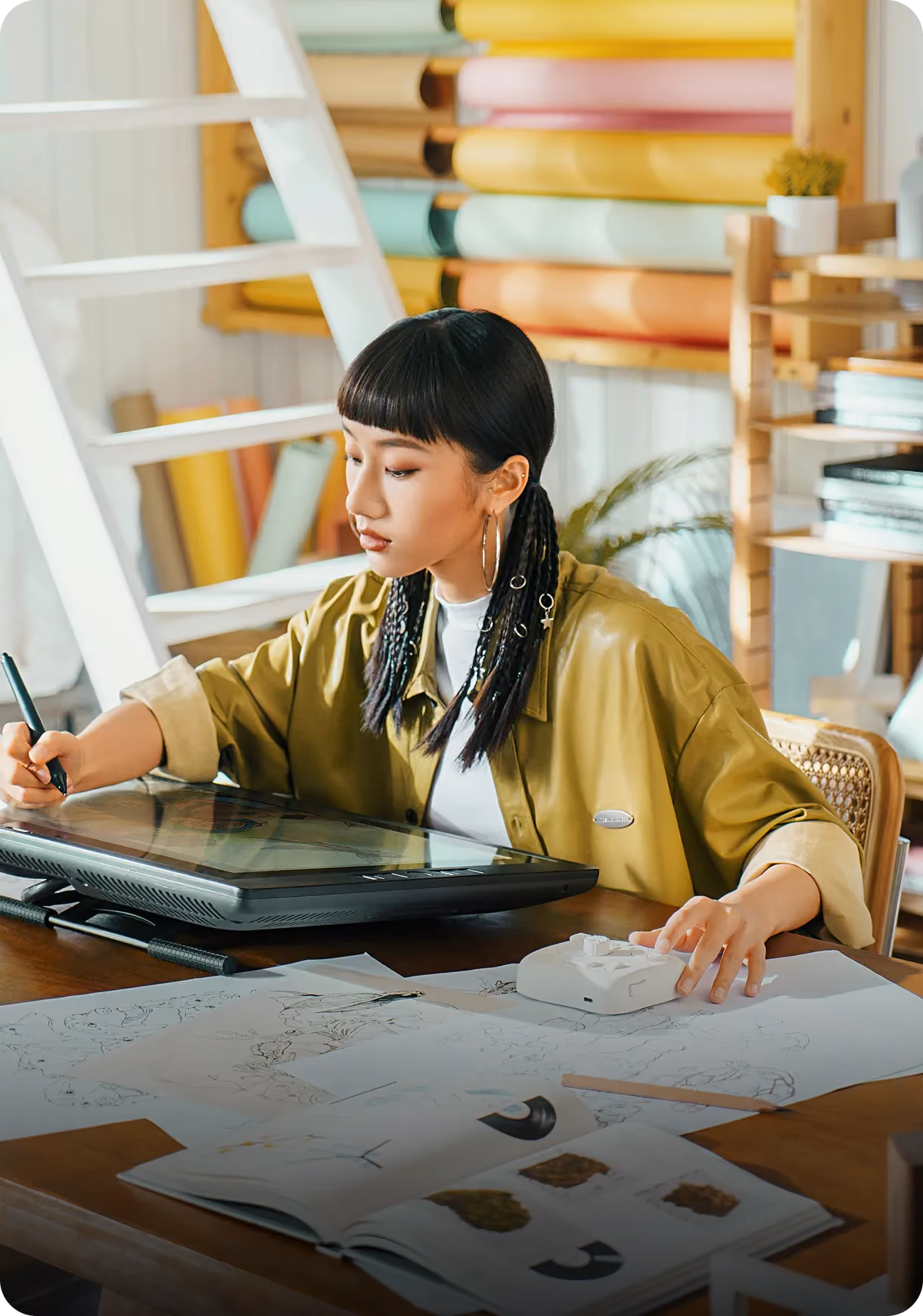 Young woman using a pen tablet for digital drawing at a desk with sketches and books.