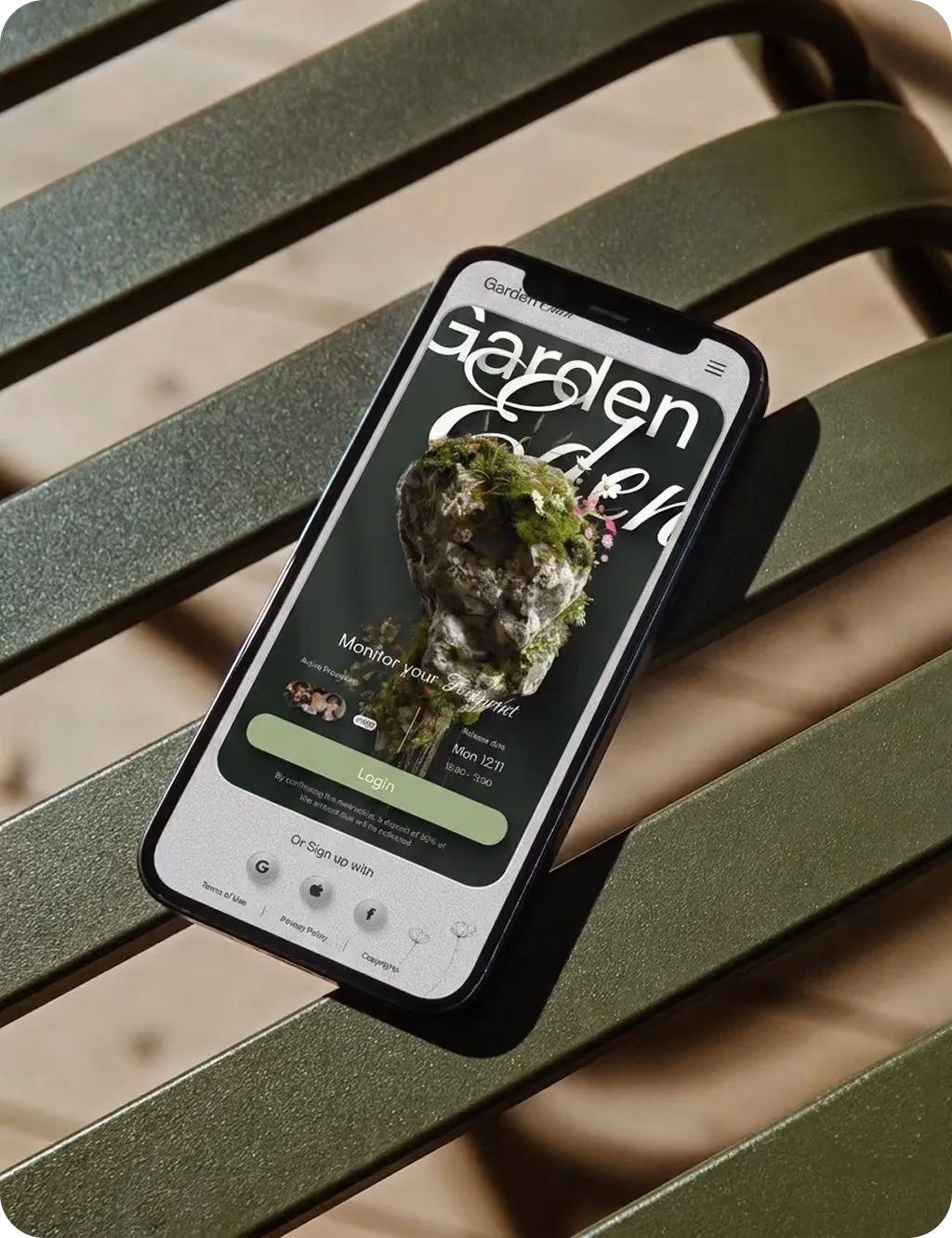 Smartphone on green bench displaying a garden-themed app with login button and mossy rock image.