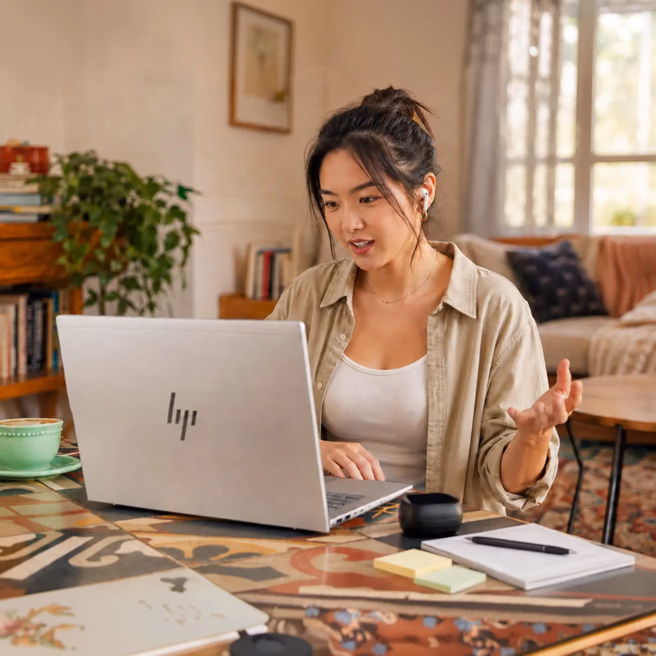 Young woman wearing earbuds engaging in a video call on a laptop at a decorated table.