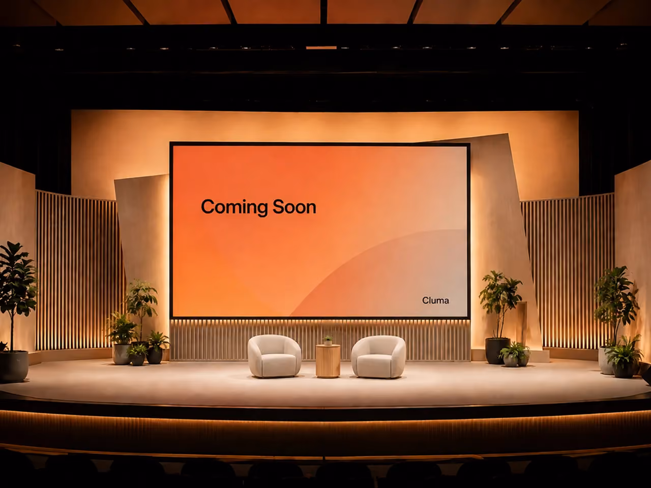 Stage with two white chairs, small table, plants, and a screen displaying 'Coming Soon'.