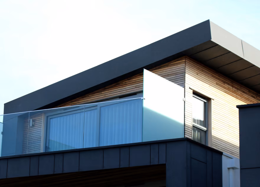 Modern house corner with wood paneling, large window, glass balcony, and black trim roof.