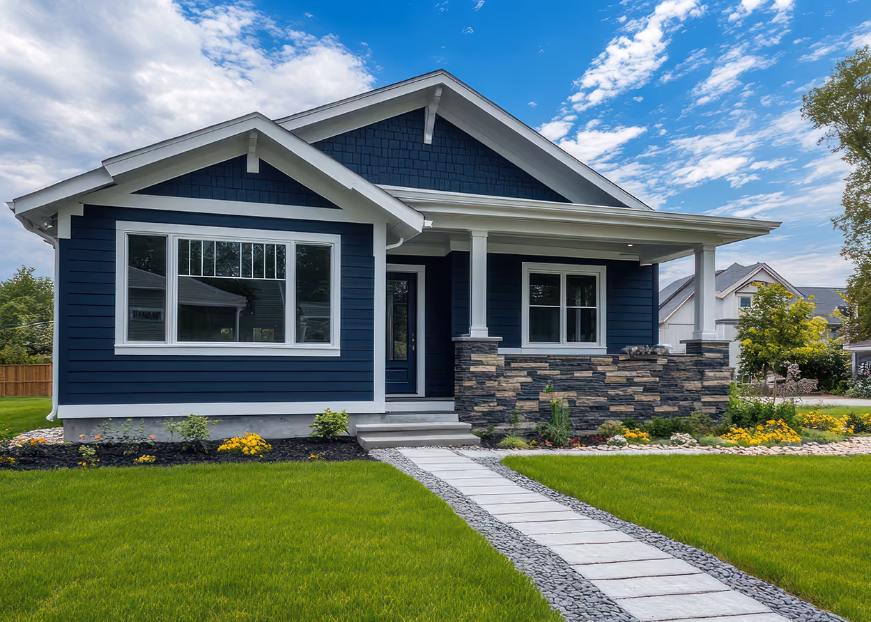 Blue house with white trim, stone porch, and a paved walkway on green lawn under a partly cloudy sky.