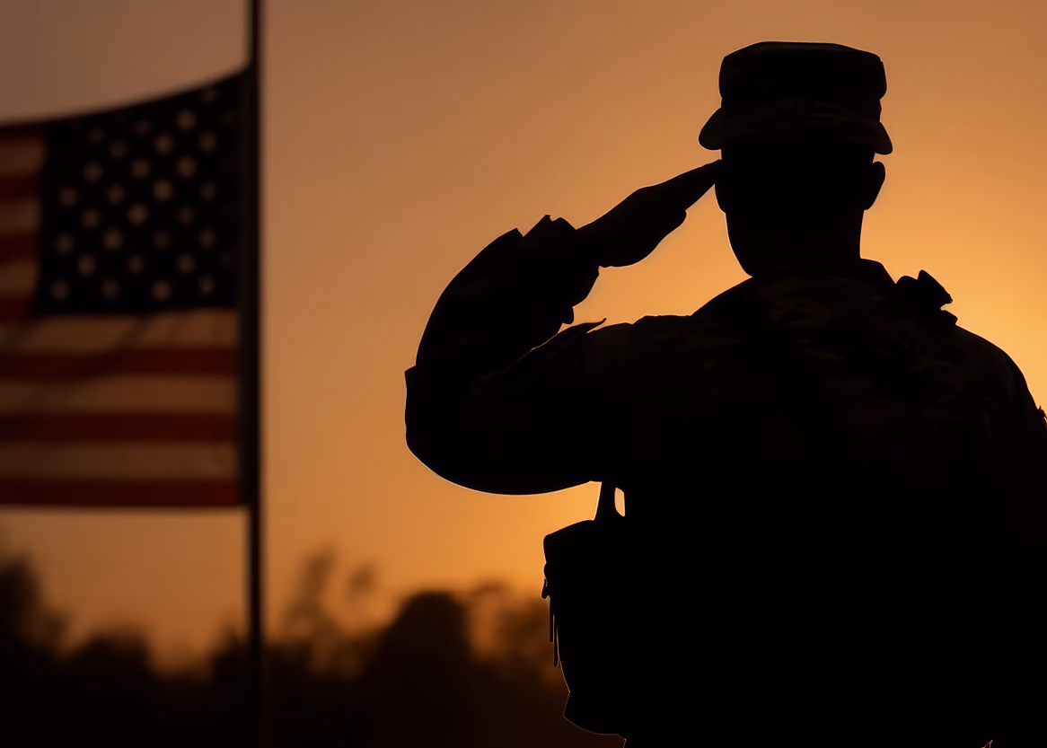 Silhouette of a soldier saluting with a U.S. flag in the background at sunset.