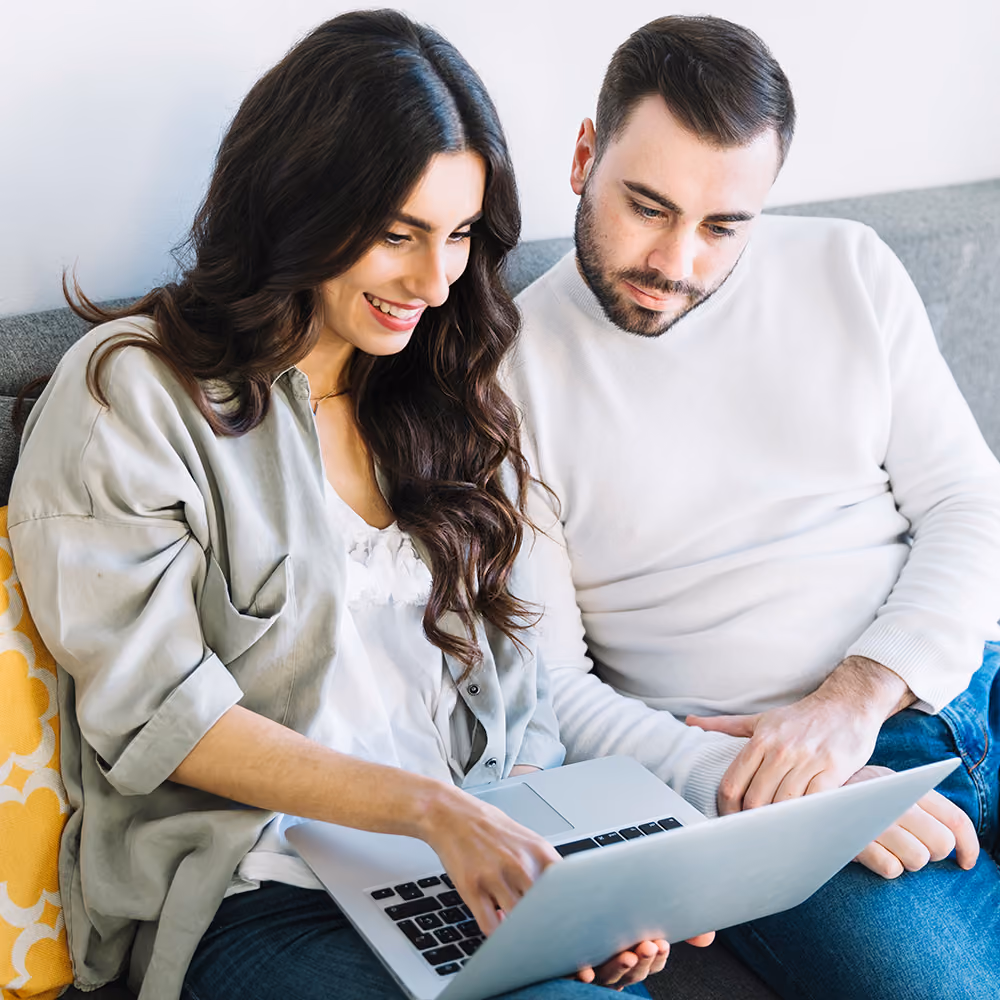 Smiling woman and man sitting on couch looking at a laptop screen together.