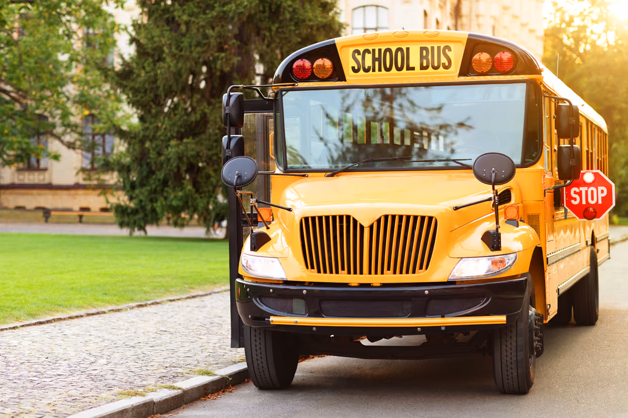 Front view of a yellow school bus with stop sign extended parked near a green lawn and trees.