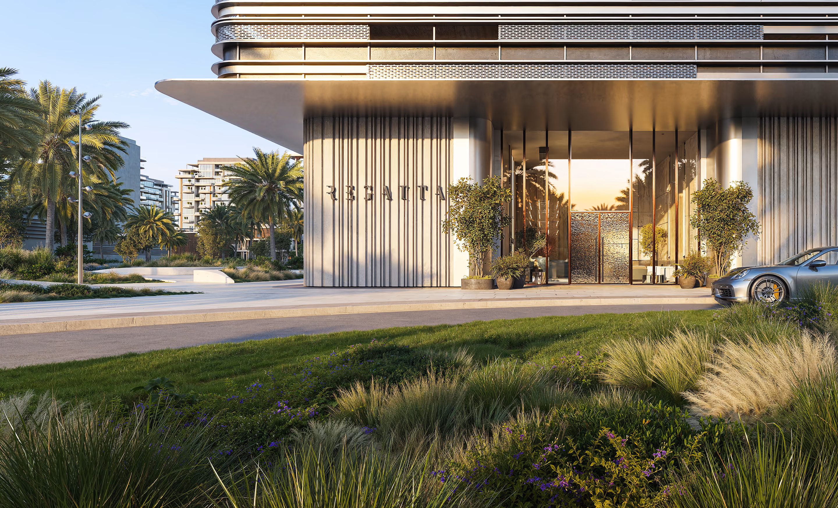 Modern building entrance with plants, palm trees, and a silver sports car parked on the right.