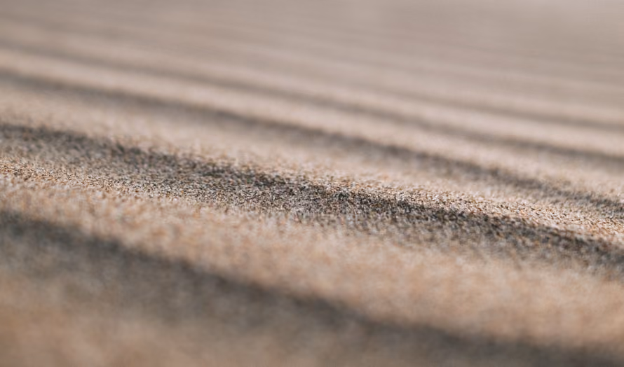 Close-up of sand with fine ridges, creating a textured pattern of light and shadow.