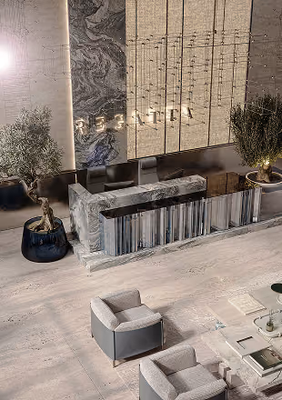 Modern lobby with marble reception desk, two gray armchairs, and potted olive trees.