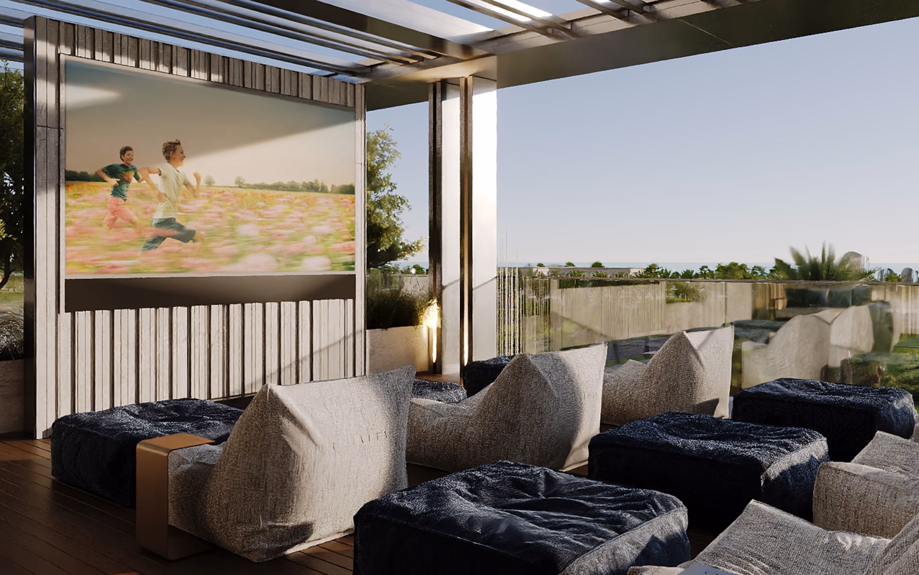Outdoor seating area with cushioned chairs and bean bags facing a large screen showing children running in a field.