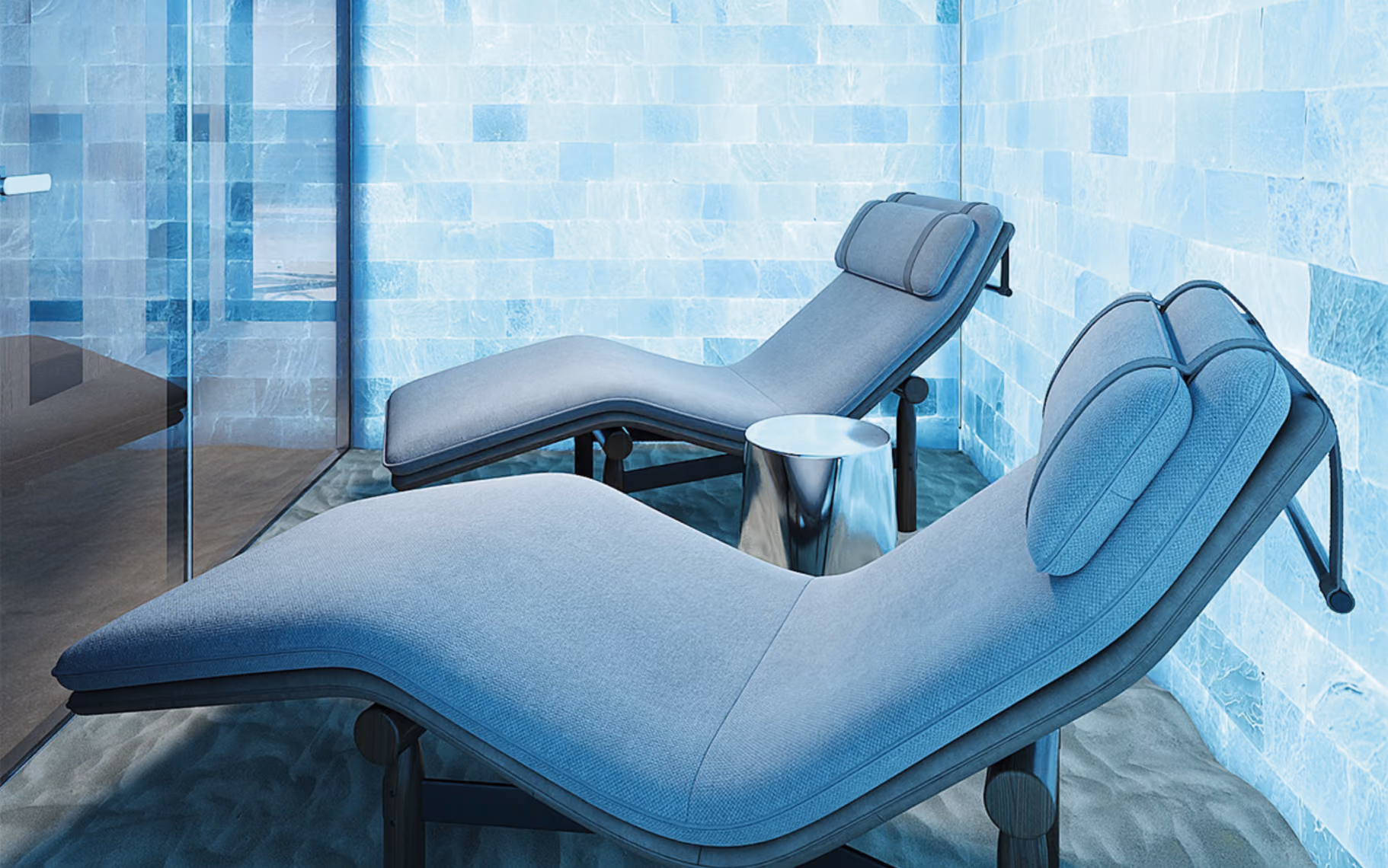 Two modern gray lounge chairs and a small metallic table in a room with light blue tiled walls.