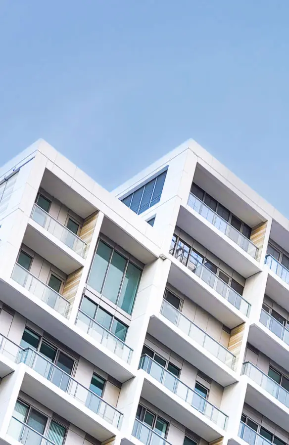 Modern white apartment building with multiple balconies and large windows under a clear blue sky.
