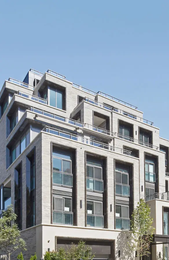 Modern multi-story residential building with large windows and multiple balconies under a clear blue sky.