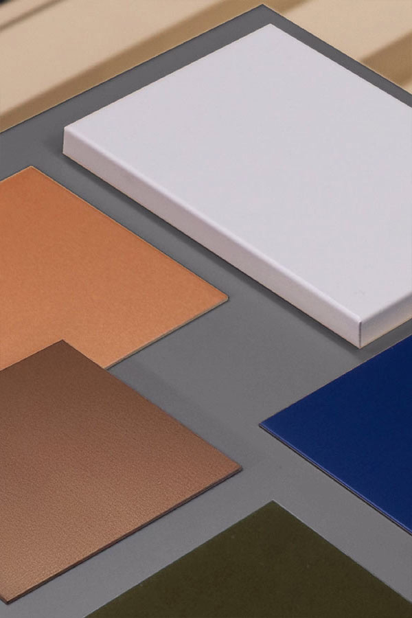 Close-up of six rectangular aluminum surface samples in different colors arranged on a gray background, including white, light brown, dark brown, blue, and green shades.