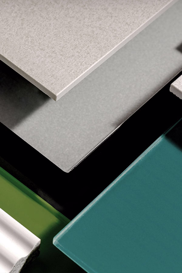 Close-up of various flat surface materials in different shades including beige, gray, black, green, and teal, arranged overlapping each other on a dark background.
