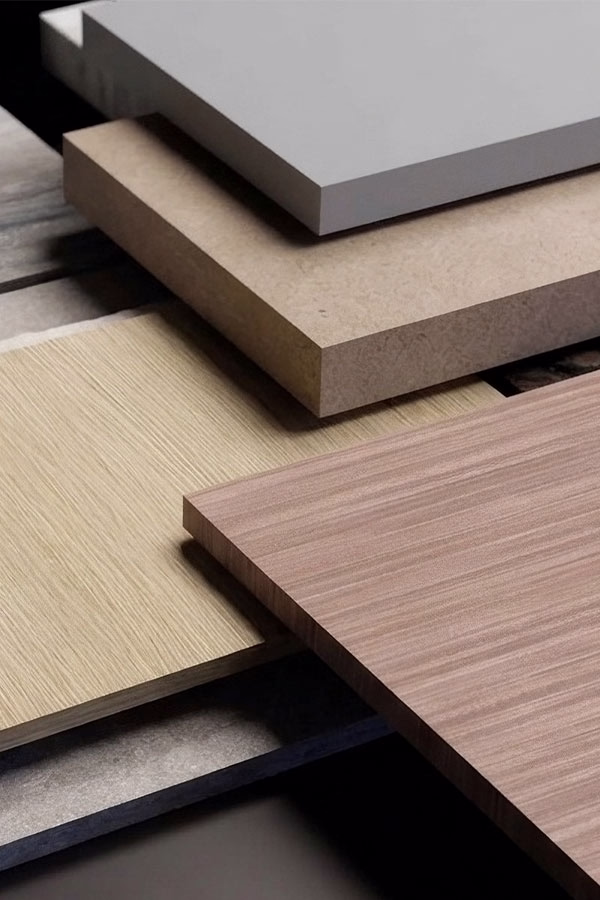 Four rectangular samples of home surface materials stacked and arranged, including a smooth white sheet, a textured beige panel, and two wood grain panels in light and medium brown tones.