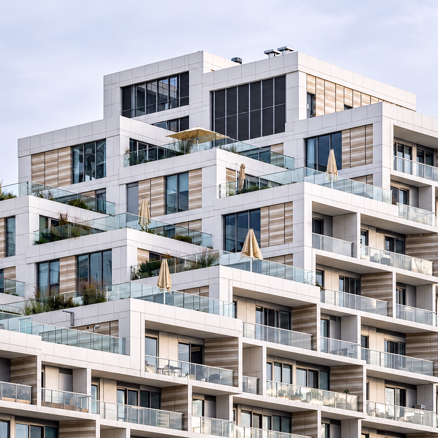 Modern multi-story residential building with staggered terraces featuring glass railings, beige umbrellas, and decorative plants.