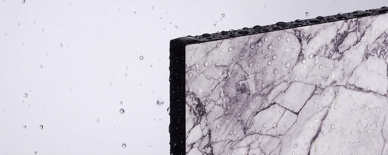 Close-up of a marble-patterned rectangular surface edge with water droplets on it and droplets falling nearby against a plain background.