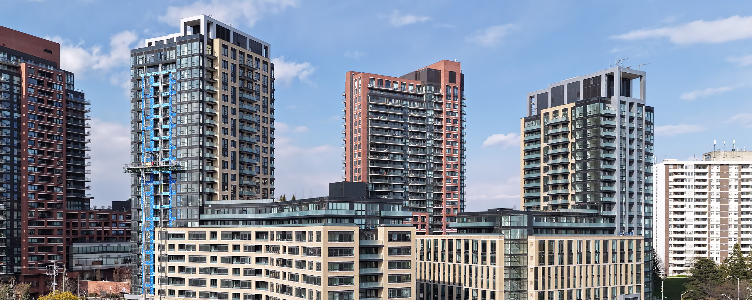 Cluster of modern high-rise residential buildings under a partly cloudy blue sky in an urban setting.