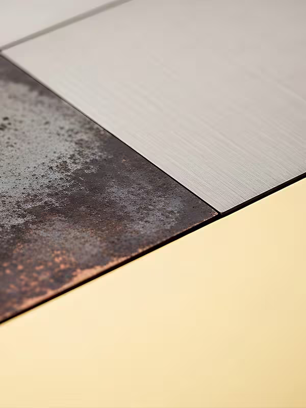 Close-up of three metal panels with different textures and finishes: one rusted and weathered, one brushed aluminum, and one smooth light gold.
