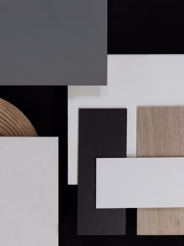 Overhead view of various rectangular and square samples of materials and colors including gray, black, white, light wood texture, and a round wood-textured piece on a black background.