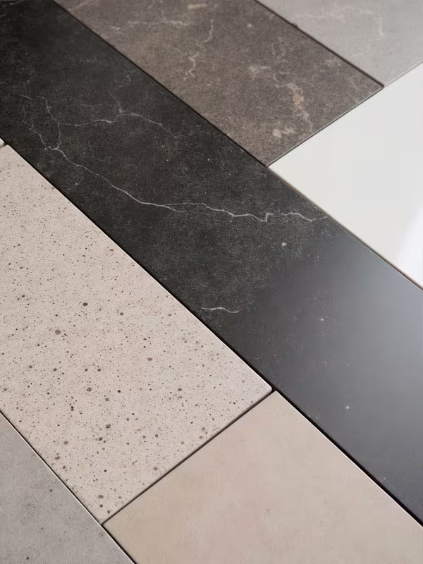 Close-up of rectangular porcelain tiles arranged in a staggered pattern, featuring various shades of gray, beige, and black with different textures including smooth, speckled, and marbled surfaces.