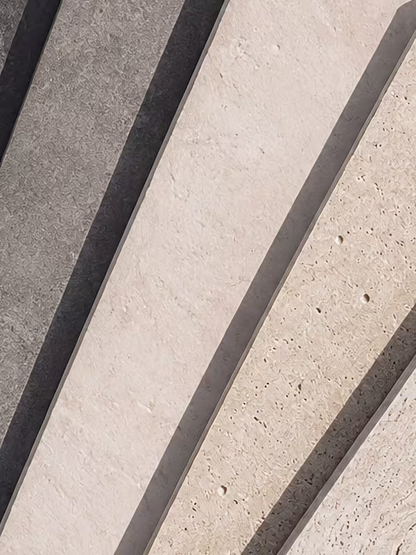 Close-up of six textured rectangular stone slabs arranged in a row with shadows in between, colors ranging from dark gray to beige.