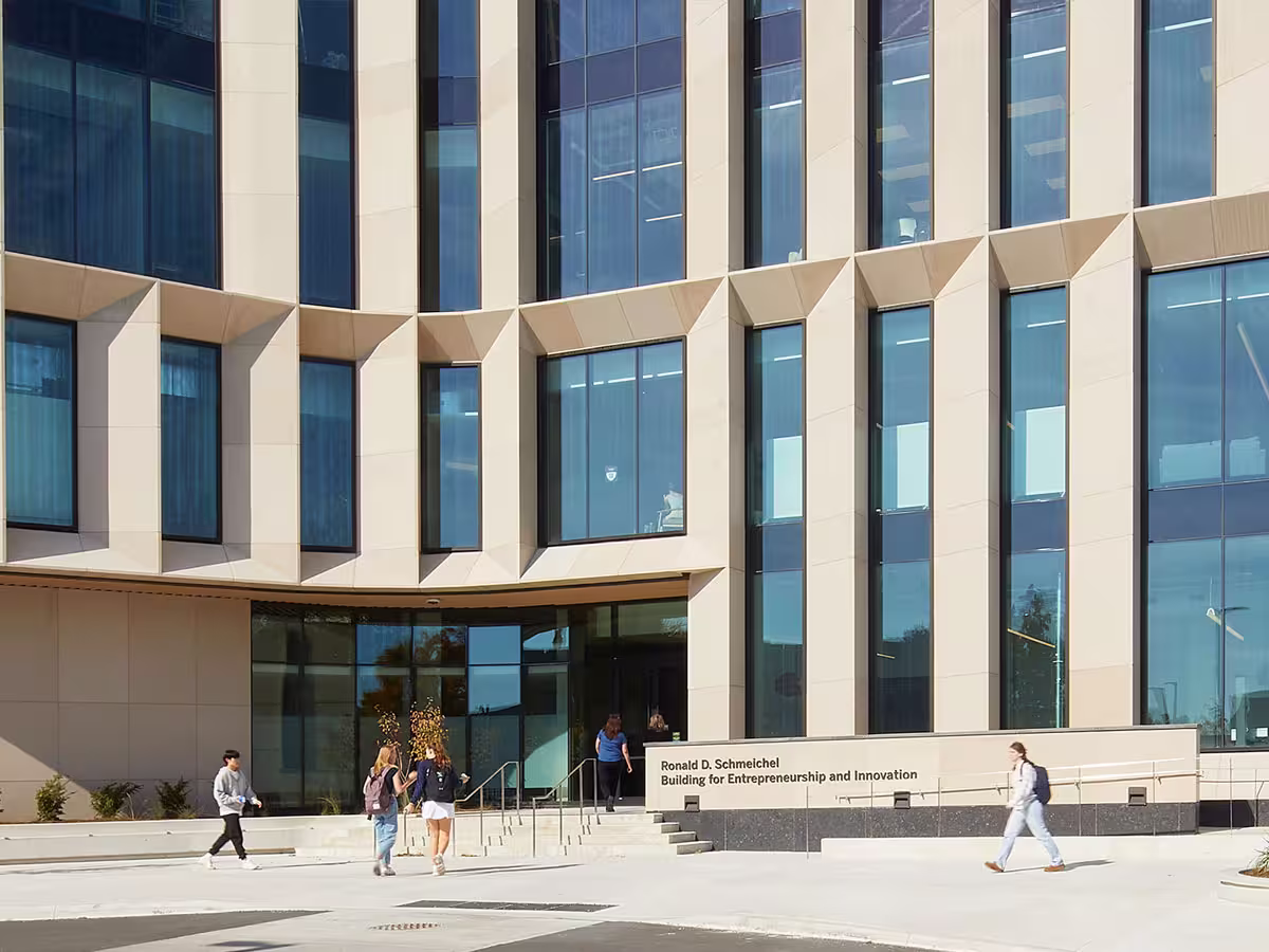 The Ronald D. Schmeichel Building for Entrepreneurship and Innovation with modern beige and glass facade, people walking near its entrance on a sunny day.