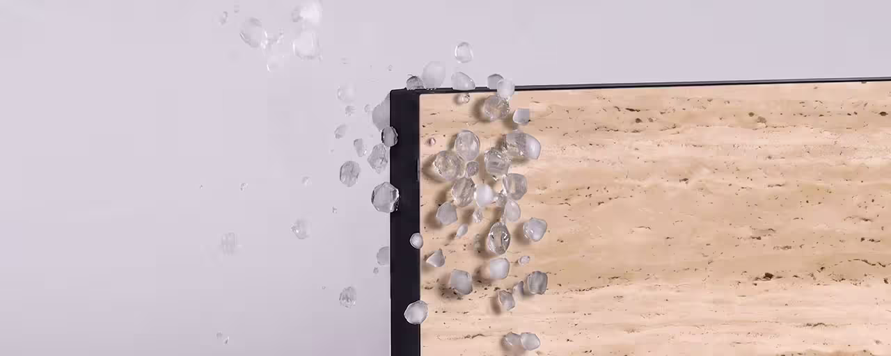 Close-up of small translucent hailstones bouncing off the edge of a beige stone surface with a black border.