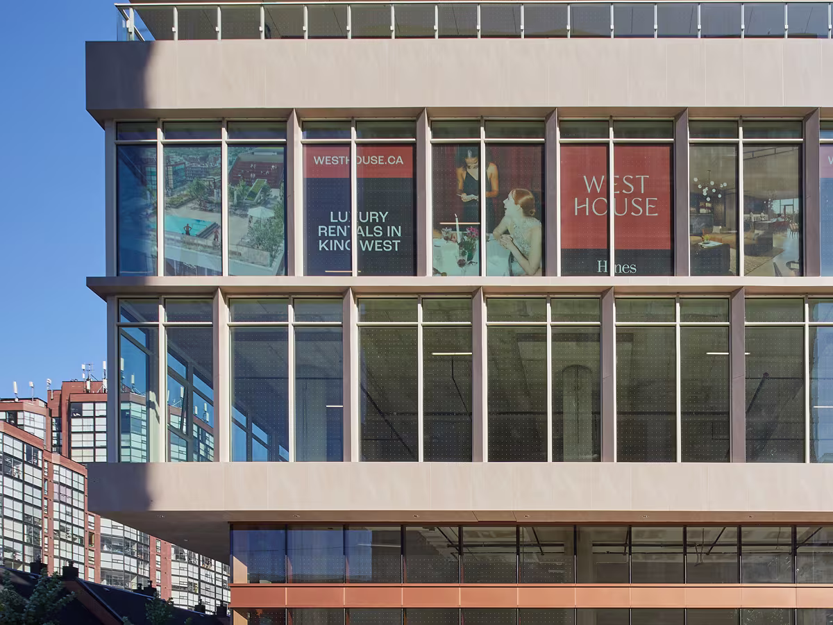 Modern building facade with large glass windows displaying advertisements for West House luxury rentals in King West, showing images of interiors and people inside.