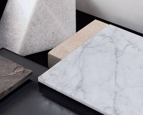 Close-up of various stone and marble surfaces including a white marble slab with gray veins, a beige textured stone piece, and darker stone samples on a black background.