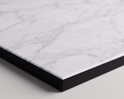 Close-up of a rectangular white marble slab with subtle gray veining and a sharp black edge, resting on a light surface.