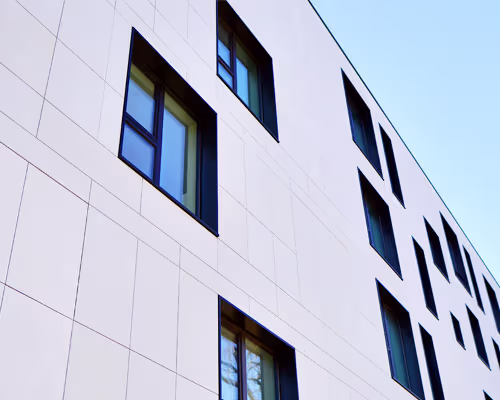Modern white building facade with large rectangular windows of varying sizes under a clear blue sky.
