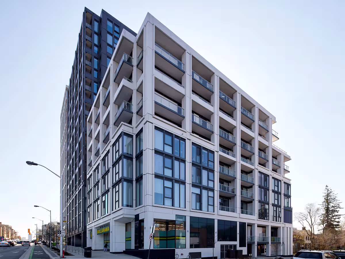 Modern mid-rise building with white exterior and glass balconies at the corner of a city street, featuring a ground-level Dollarama store.