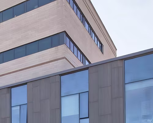 Close-up view of a modern building facade featuring large blue-tinted glass windows and light-colored stone panels with clean, geometric lines.