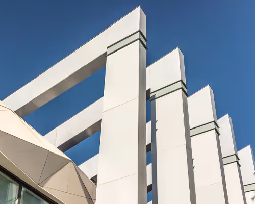 Modern architectural detail of white vertical pillars and beams set against a clear blue sky.