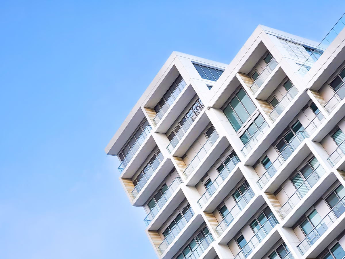 Modern white residential building with multiple glass balconies against a clear blue sky.