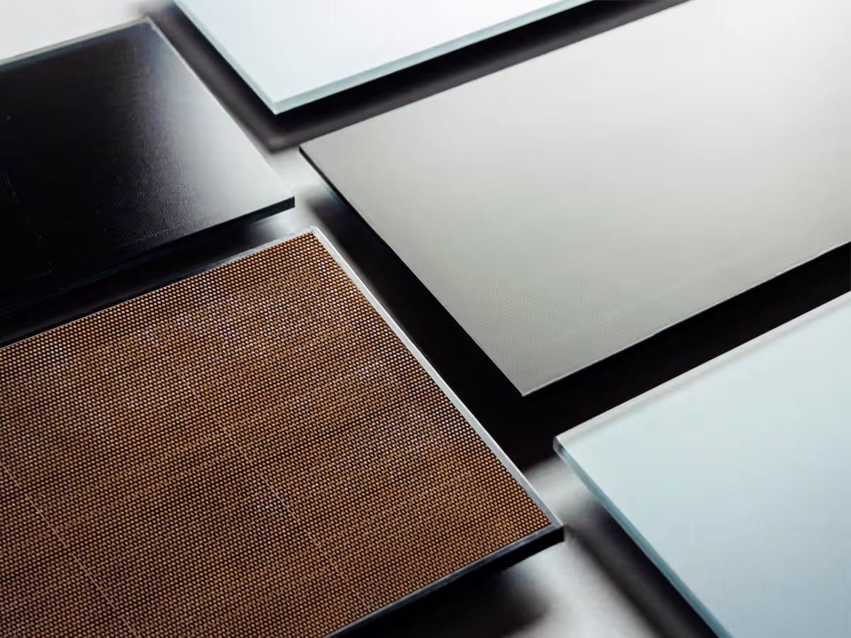 Close-up view of various flat solar panel materials arranged in a grid, including a brown textured photovoltaic cell and smooth glass and metal sheets.