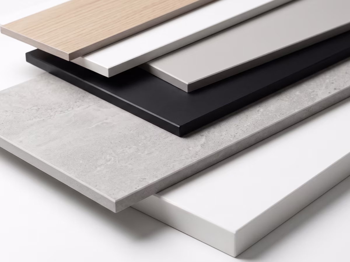 Six stacked rectangular tiles showcasing different finishes and colors, including light wood, white, gray, black, concrete texture, and plain white, laid out diagonally.