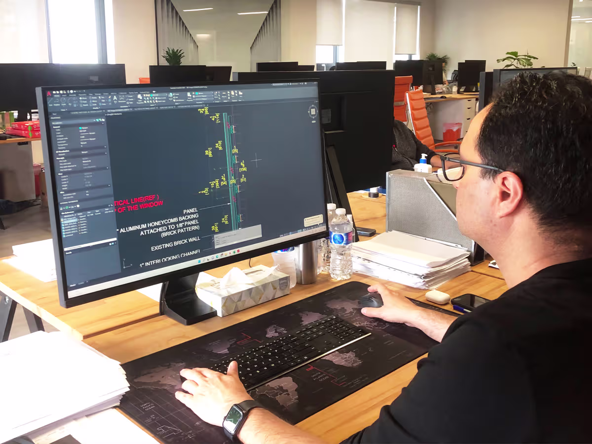 Person working on a computer in an office setting, viewing a detailed architectural or engineering drawing with annotations on the screen.